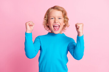 Photo of small excited boy scream raise up fists wear blue turtleneck isolated pastel pink color...