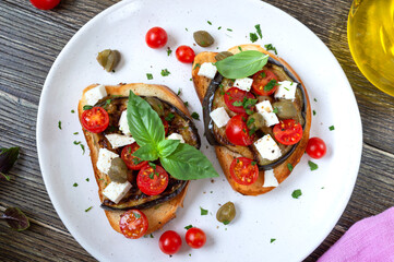 Garlic bruschetta with eggplant, feta, cherry tomatoes, capers. Useful vegetarian appetizer. Italian Cuisine.