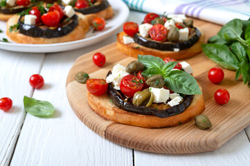 Garlic bruschetta with eggplant, feta, cherry tomatoes, capers. Useful vegetarian appetizer. Italian Cuisine.