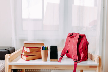 School supplies on the school desk. Red backpack, white headphones, notebook, big red books, pens in the jar lay on the white school desk. - Powered by Adobe