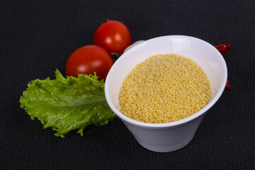 Raw couscous in the bowl served salad leaves, tomato and pepper