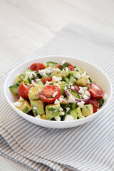 Tasty Avocado Tomato and Cucumber Salad in a bowl on a white wooden surface, side view. Close-up.