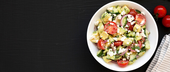 Delicious Avocado Tomato and Cucumber Salad in a white bowl on a black surface, top view. Flat lay, overhead. Space for text.