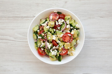 Tasty Avocado Tomato and Cucumber Salad in a bowl on a white wooden background, top view. Flat lay, overhead, from above.