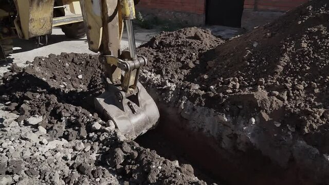 Big metal excavator bucket scoops up dirt while digging a ditch during roadworks in countryside. Ripper bucket excavating soil and rocks at a construction site on a sunny day.