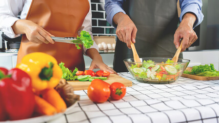 Happy couple having fun standing in kitchen at home preparing vegetable salad husband and wife vegetarians chop vegetables prepare for dinner in loft kitchen at home.