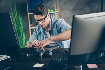 Photo of smart expert guy repairman master fix airplane drone use equipment sit desk in modern...