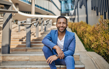 Obraz premium Smiling handsome Indian arabic business man sitting on outdoor city staircase