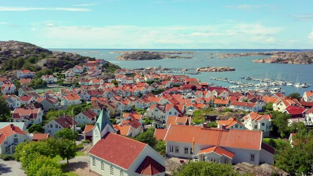 Drone shot over town in Sweden. Aerial view of Swedish houses with red roof tops on west coast bohuslan. Summer day by the ocean at Bovallstrand holiday vacation destination. Tourist and sailing boats