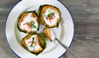 Steamed fish with curry paste in banana leaf cup and *Yor leaves (Thai herb)* in white dish  (Thai language called Hor mok) on old wooden table which has black background
