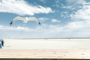 Wooden plate and blurred outdoor photo. Sunny day on sandy beach, seagull and sky.