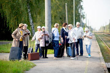 A group of positive senior elderly people travelers using tablets waiting for train before going on...