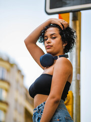 Brazilian woman with headphones in the street. woman sitting on the roof with a modern building in the background