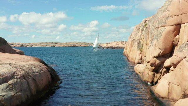 Sailing boat in Sweden between islands on swedish west coast. Aerial drone shot on sunny summer day perfect archipelago weather. Bohuslan granite rocks cruising ship or boat on ocean at shoreline
