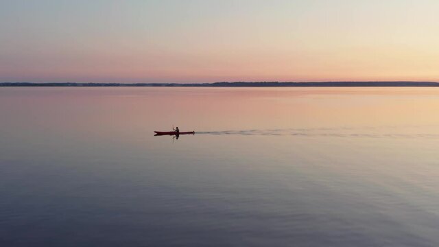 Kayak paddle on lake at sunset. Calm water evening light outdoor activities on canoe. Aerial drone shot magical night on the water. Small ripple waves. Single person rowing in boat in nature.