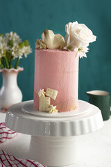 Vertical closeup shot of a small fancy pink cake with white roses on a tray