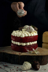 Vertical shot of a person pouring sugar powder on a fancy small red velvet cake with white cream