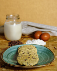 Vertical shot of chocolate chip cookies next to a jar of milk, on a wooden surface