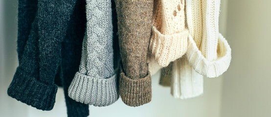 Knitted clothes sweater hanging in the closet. Cozy autumn-winter wardrobe. Banner image