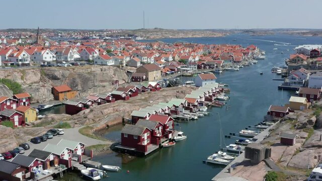 Swedish town on the west coast of Sweden in summer time. Smogen Bohuslan ocean canal with small tiny red wooden cabin houses boats and residential home in aerial drone view. Kungshamn in background