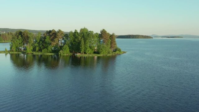 Swedish lake archipelago and small island in aerial drone view. Blue water and green trees on warm summer evening. Dalarna Sweden