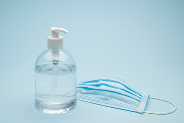 Dispenser of antibacterial gel with surgical mask on blue background