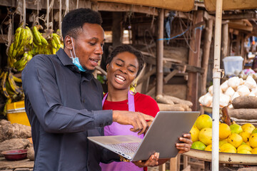 young man with a laptop showing something to a woman in a local african market