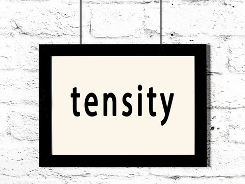 Black frame hanging on white brick wall with inscription tensity