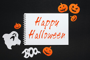 Happy halloween holiday concept. Notepad with text Happy Halloween on black background with bats, pumpkins and ghosts