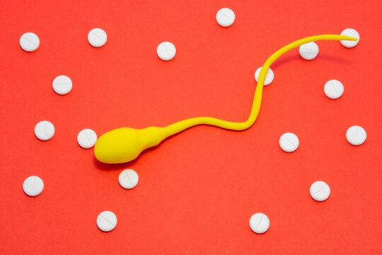 3D anatomical model of sperm cell or spermatozoon is on red background surrounded by white pills ornament polka dots. Photo concept of treatment of sperm diseases, cell pathology, male infertility