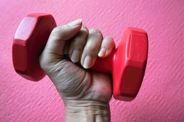 A woman's hand pressing a red dumbbell against a bright red background.