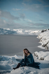 Fototapeta na wymiar Young woman posing sitting in snow on a beautiful sunny winter day next to a frozen lake