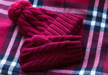a knitted hat with a pom-pom and red mittens lie on a checkered scarf. Warm set. Winter, Christmas, cute and useful, gifts. Knitted set as a gift