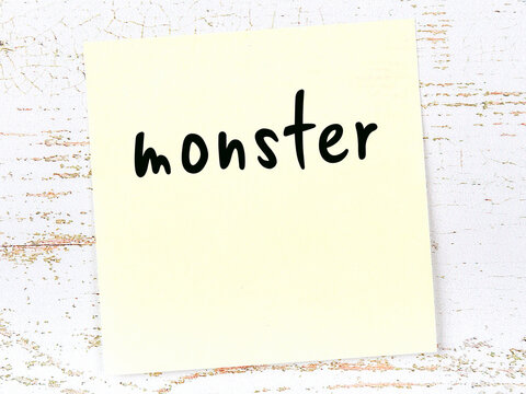 Yellow sticky note on wooden wall with handwritten word monster