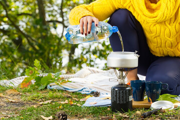young beautiful girl in a yellow sweater makes coffee in the forest on a gas burner. Making coffee on a primus stove in the autumn forest step by step
