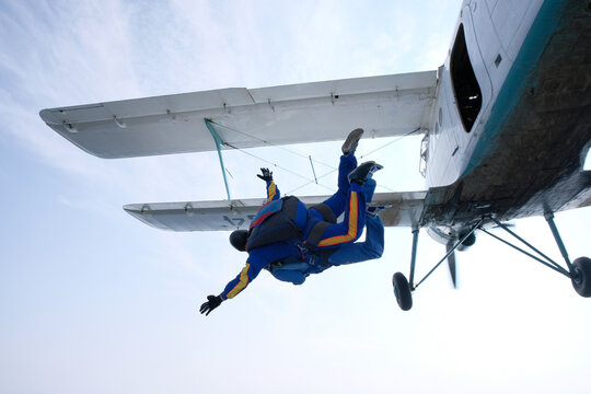 Skydiving. A tandem has just jumped out of a white biplane.