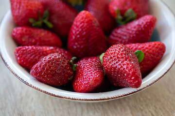 Close-up on a bowl with strawberries on a wooden table.