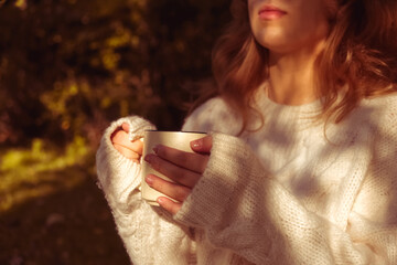 girl in a warm white sweater holds Cup of coffee. Autumn background, the concept of warmth and comfort