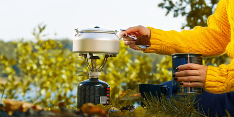 young beautiful girl in a yellow sweater makes coffee in the forest on a gas burner. Making coffee on a primus stove in the autumn forest step by step