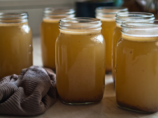 Home made bone broth in glass jars on kitchen table. Natural light.
