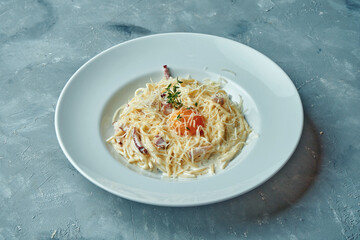 Italian pasta carbonara with bacon, creamy sauce and yolk, cheese in a white plate on a gray background