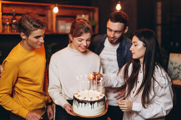 attractive teenage girl celebrating her birthday with cake together with best friends who decided to surprise her and unexpectedly greet her at a holiday party in home
