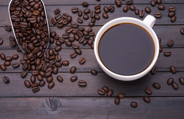 Dark coffee in a white coffee cup and roasted coffee beans placed on a black wooden table and there is space for text design.