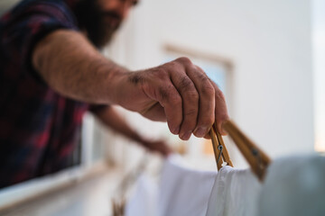 Close up of a man hanging his clothes using wooden clothespins