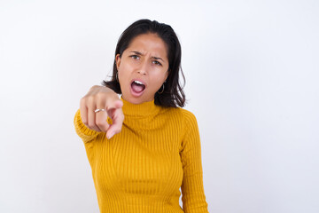 Young hispanic girl with short hair wearing casual yellow sweater isolated over white background pointing displeased and frustrated to the camera, angry and furious ready to fight with you.