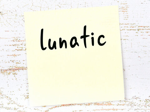 Yellow sticky note on wooden wall with handwritten word lunatic
