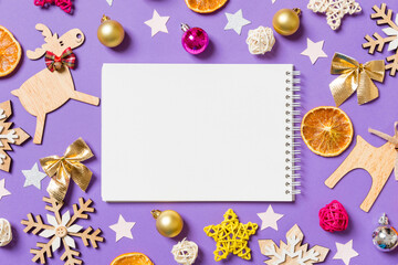 Top view of notebook surrounded with New Year toys and decorations on purple background. Christmas time concept