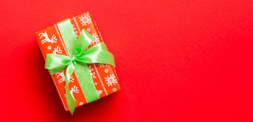 Gift box with green bow for Christmas or New Year day on red background, top view with copy space