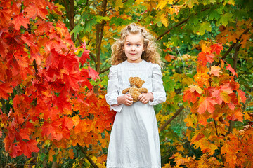 autumn portrait of a little little girl in a white dress with a toy teddy bear in her hands