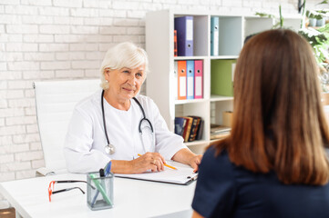 Senior female doctor looks on patient with an empathy and care. Doctor visit concept